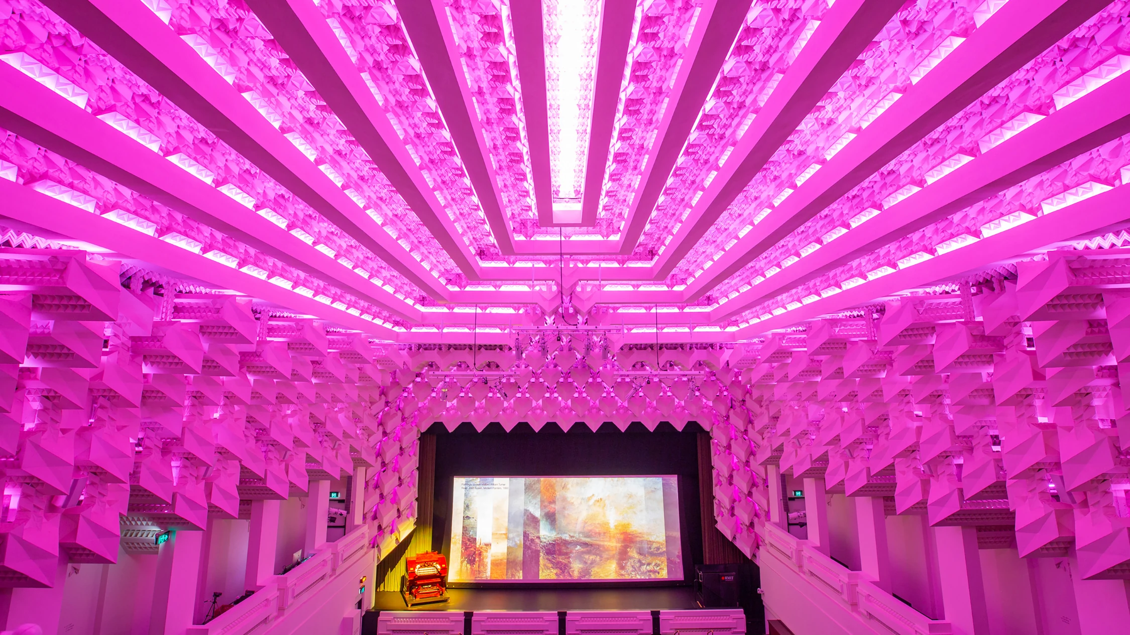 An art deco theatre ceiling lit in pink