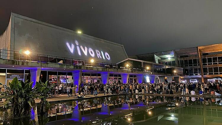 Imagem do Vivo Rio à noite, com letreiro iluminado e várias pessoas na entrada