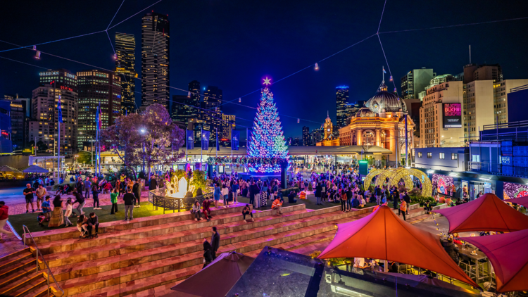 Federation Square decorated for Christmas, with a brightly lit tree and view of Flinders Street Station