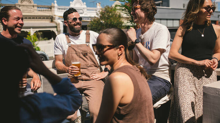 A group of people smiling outdoors with pints of beer in hand.