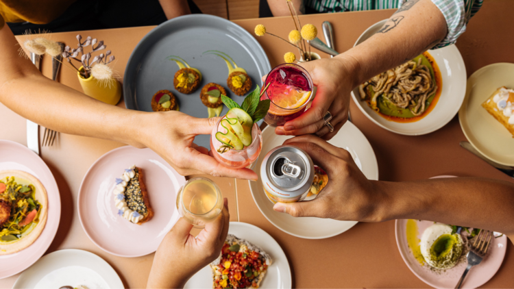 People clinking cocktails over a food spread
