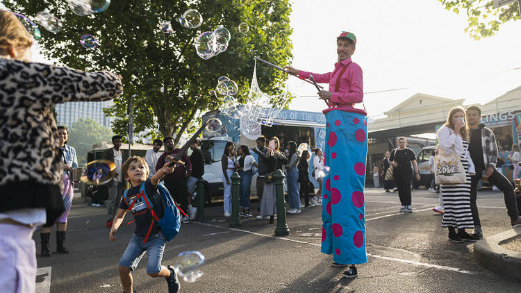 A children's entertainer on stilts blowing giant bubbles. 