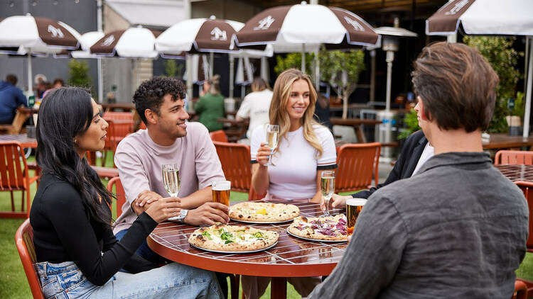 A group of people sitting at a table with pizzas and drinks.