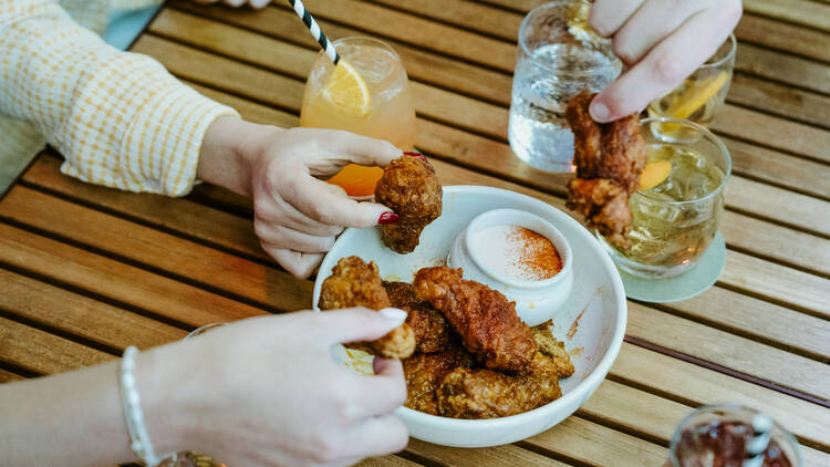 People dipping fried chicken into sauce at a table with gin cocktails.