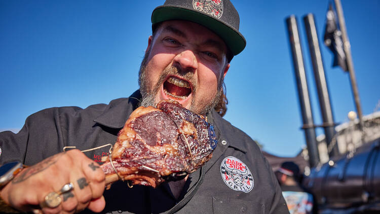 Man with grills scowling at the camera with a large piece of meat.