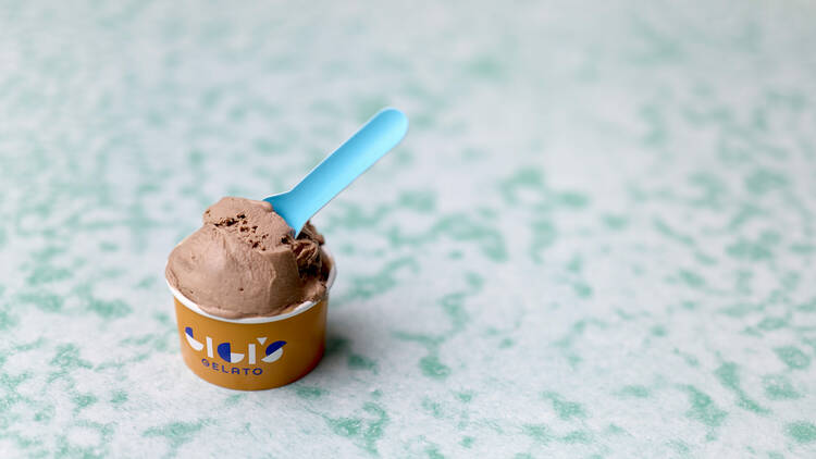 Small cup of chocolate gelato with a blue spoon. 