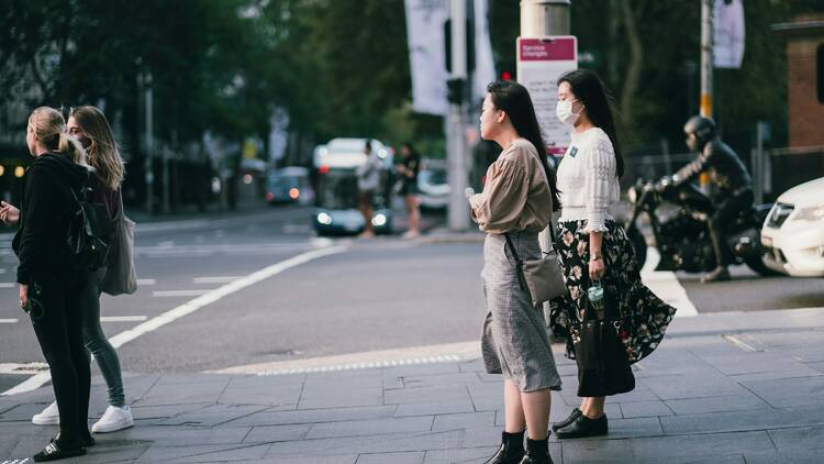 People standing at a traffic light on a Sydney city street, one wearing a mask.