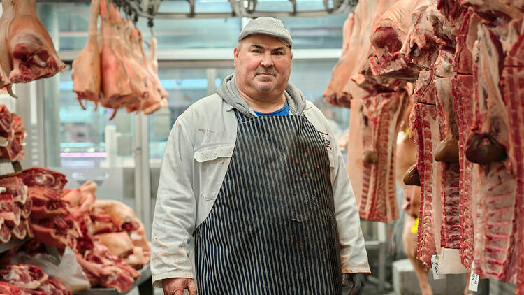 A butcher standing next to meat 