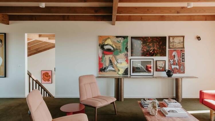 The interior of a sitting room with pink chairs and several paintings on the wall. 