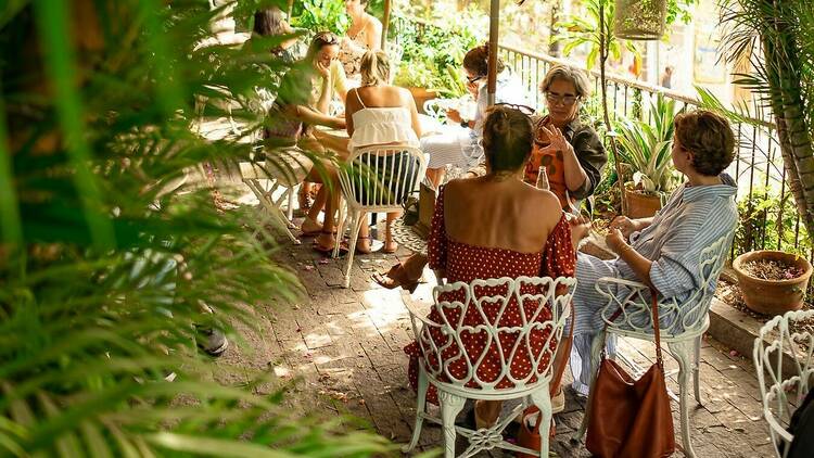 Pessoas sentadas em mesas em uma varanda cheia de verde