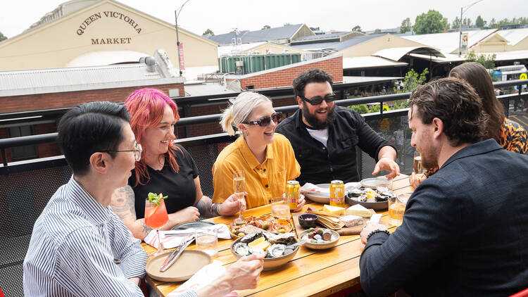 Group of people gathered around a table with dishes of food and drinks on the terrace at Brick Lane Market.