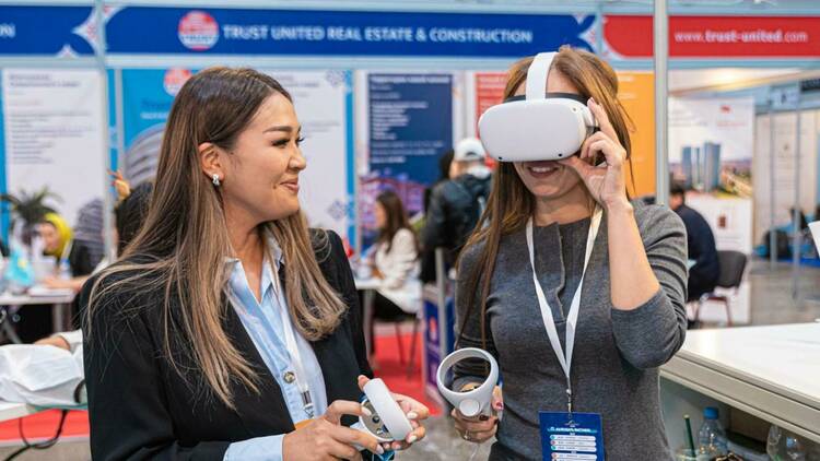 One woman letting another woman try on a VR headset