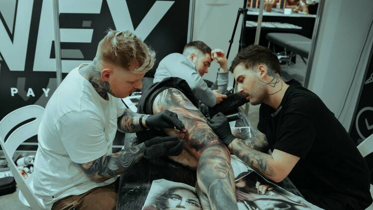 Two tattoo artists tattooing a person's leg. 