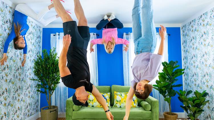 A family stand on the ceiling upside-down in a living room. 