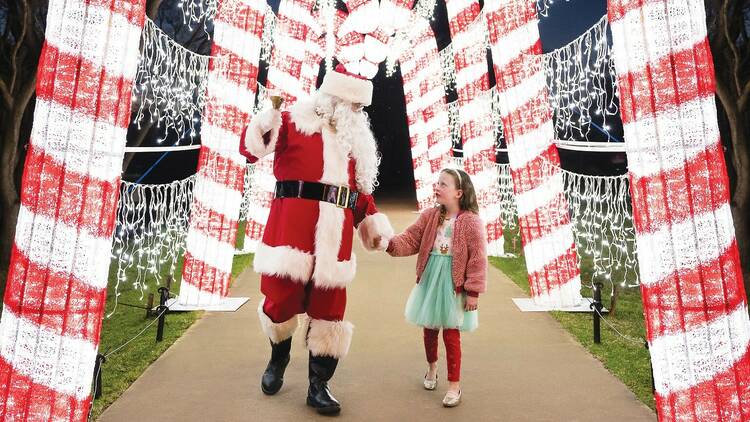 Santa holds hands with a young child under glowing candy canes