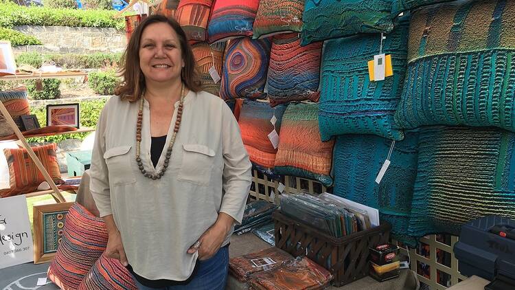 A woman stands in front of a wall of brightly coloured cushions. 