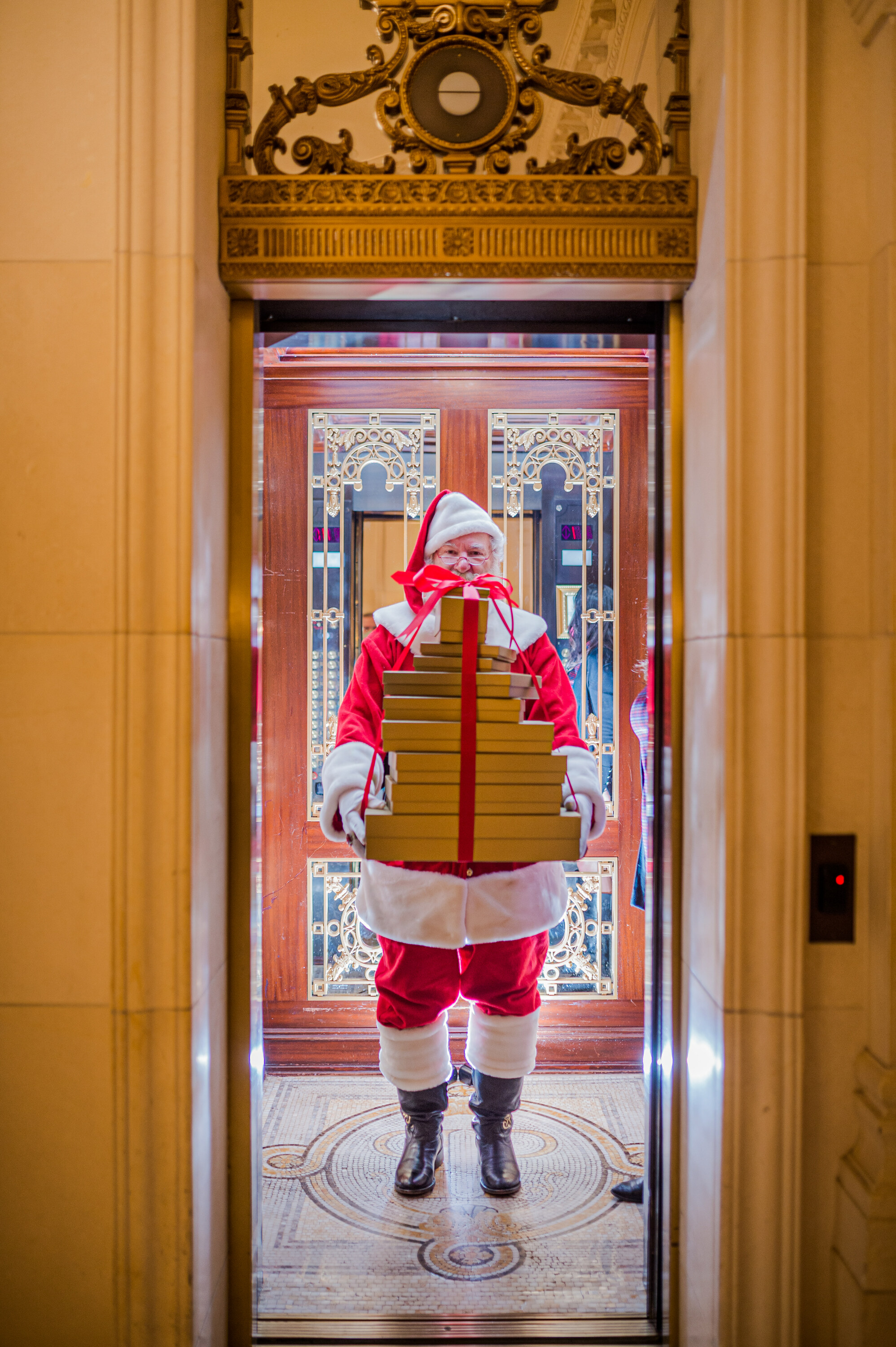 Santa holds up a bunch of gifts inside an elevator.