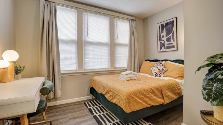 Fully decorated bedroom with orange bedspread, a desk and a plant.