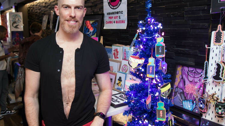A man stands next to a blue Christmas tree with ornaments for purchase.