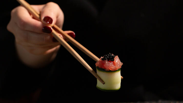 Woman with nail polish holding a piece of sushi with chopsticks.