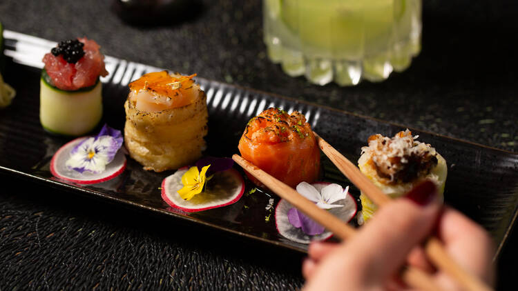 Woman picking up a piece of sushi from a colourfully garnished dish.