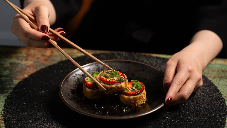 Woman picking up a piece of sushi with chopsticks.