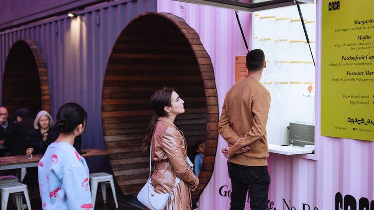 Man and woman queuing up at a pink-hued stall at Grazeland.