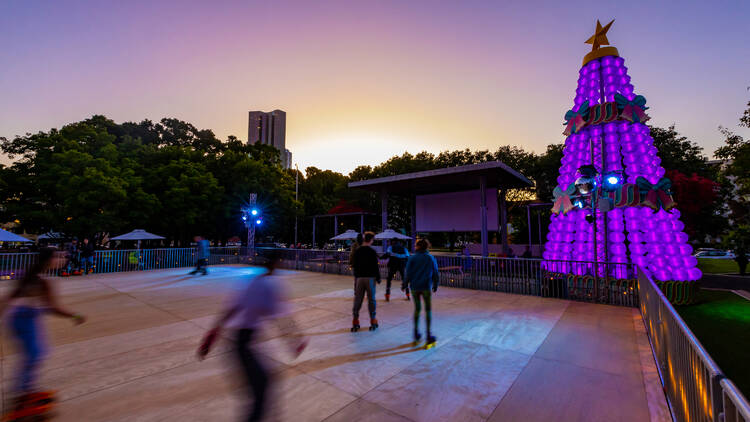 People skating on a roller rink with a colourful Christmas tree. 