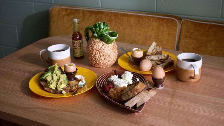An array of breakfast dishes and mugs laid out on a wooden table.