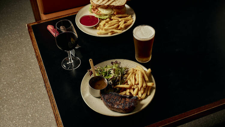 A steak and a sandwich with drinks in a pub.