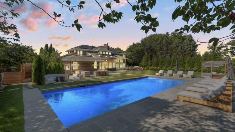 A luxury mansion in Southampton, New York, with a large outdoor pool and numerous comfortable seating areas.
