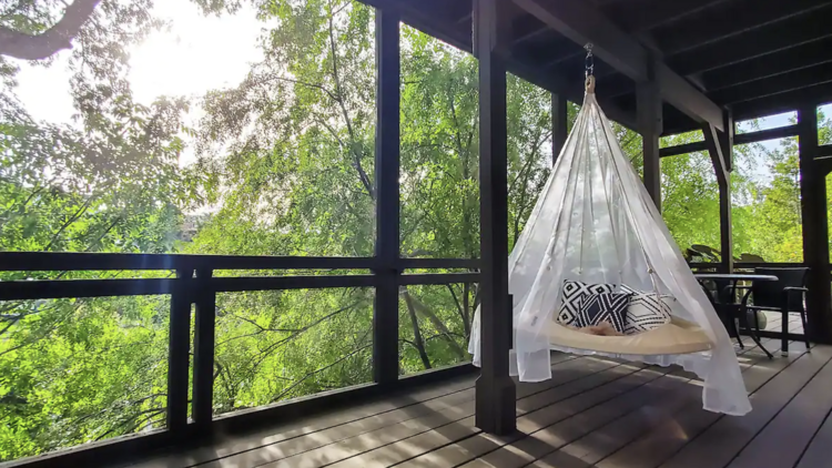 A terrace area overlooking lush green trees, complete with a swinging day bed, at an LA treehouse Airbnb.