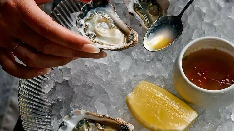 Chef spooning dressing into an oyster over ice with a wedge of lemon.