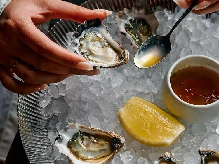 Chef spooning dressing into an oyster over ice with a wedge of lemon.