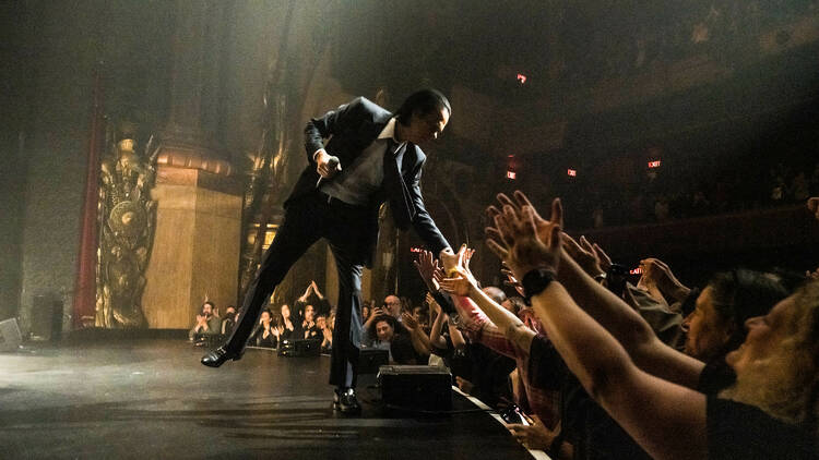 Nick Cave reaches down from stage to touch fans' hands
