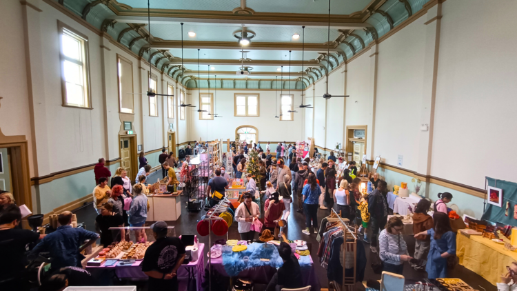Crowd browses artist stalls in a town hall for Make-it Market