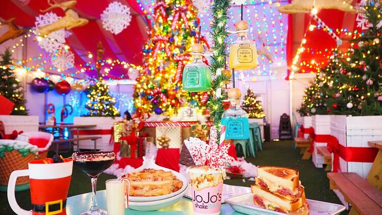 A table full of dishes and drinks in front of a Christmas tree