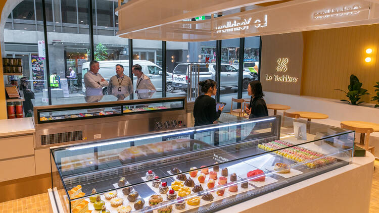 Brightly lit cake shop with display cabinets full of desserts.