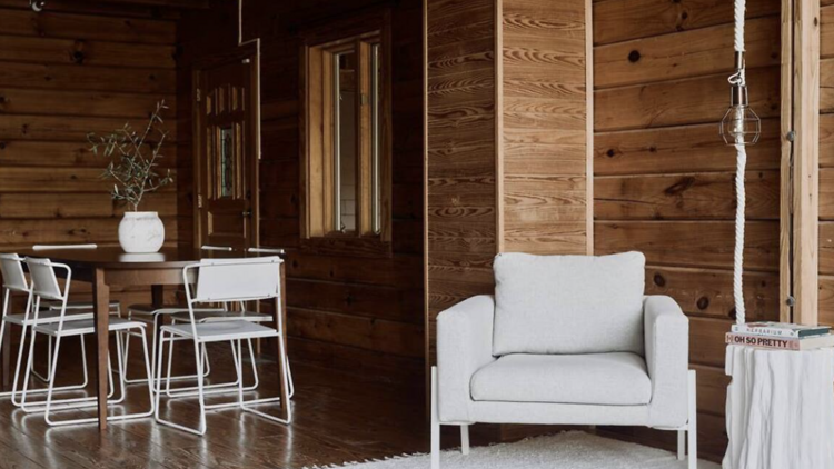 Reading corner of logwood cabin with white armchair, small table and dining  table off to the left. .