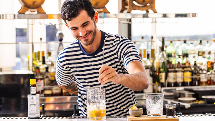 A barman in a stripy t-shirt stirring a cocktail