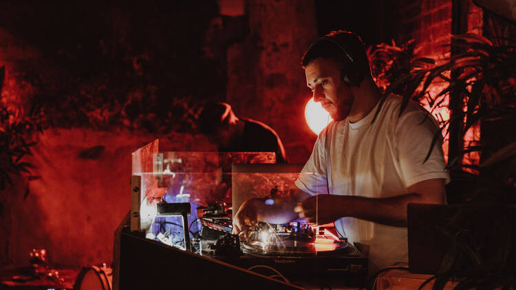 A person DJing in a red-lit room at Wax Music Lounge.