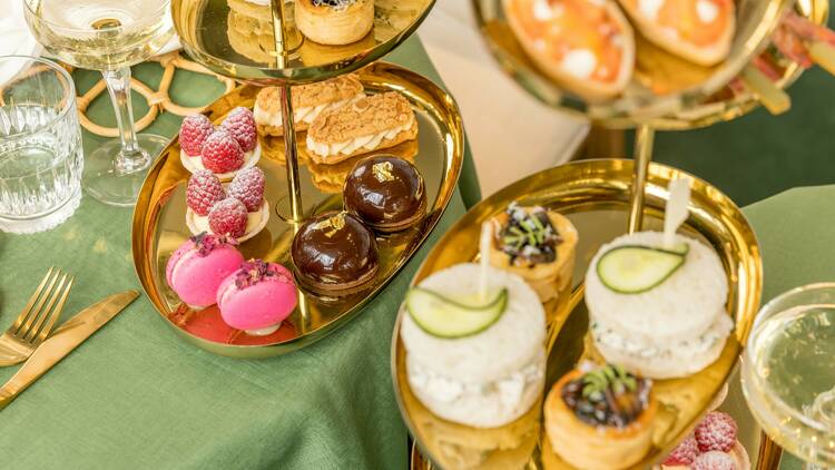 Elegant gold high tea trays filled with savoury and sweet food items. 