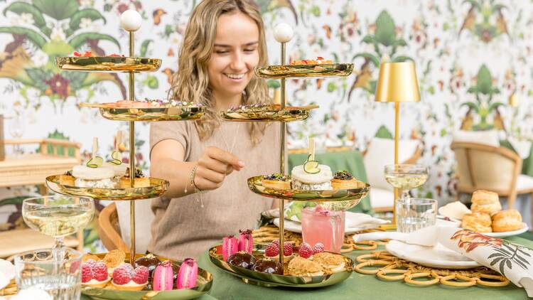 Smiling woman selecting an item from a gold tiered platter stand at a high tea.