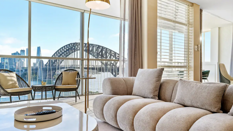 A luxury living room in a Sydney Airbnb with large floor-to-ceiling windows overlooking the Sydney Harbour Bridge.