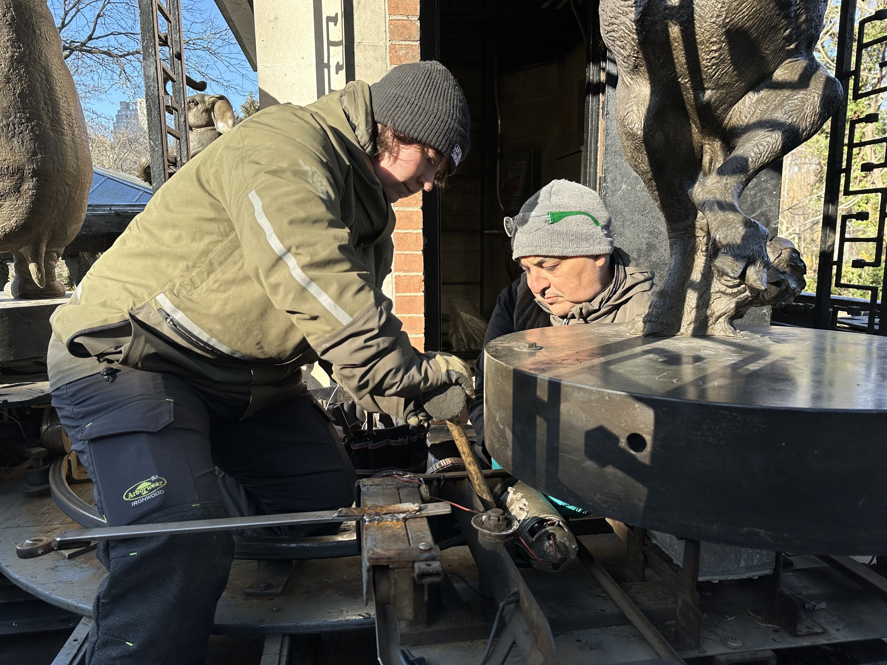 Two park technicians work on the clock.