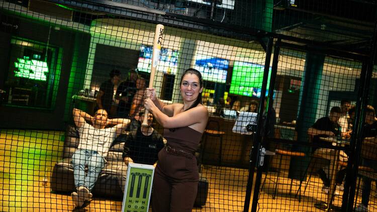 A woman in an indoor net with a baseball bat.