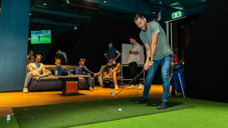 A man playing indoor golf with people watching.