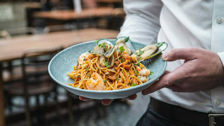 A waiter holding a bowl of seafood pasta.