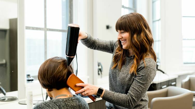 A hairdresser blow drying a woman's hair in the salon.