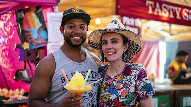 Two people pose with an icy drink at a market.